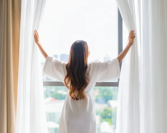 flourish () Woman opening curtains to morning light, feeling renewed
